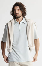 Load image into Gallery viewer, Man wearing a light gray polo shirt with a beige hooded garment over it on a white background