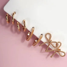 Load image into Gallery viewer, Set of gold hoop earrings on a white surface with a pink background
