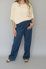 Load image into Gallery viewer, Person wearing blue jeans and a beige top on a white background
