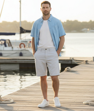 Load image into Gallery viewer, Man wearing a light blue shirt over a white t-shirt and light gray shorts on a white background
