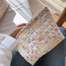 Load image into Gallery viewer, Floral quilted clutch held by a person with a neutral background
